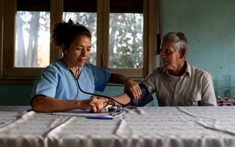 A healthcare provider checking the blood pressure of a patient while sitting at a table.