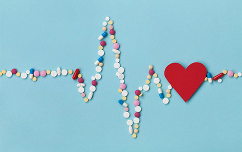 Pills arranged in the shape of a heartbeat on a blue background with a red heart