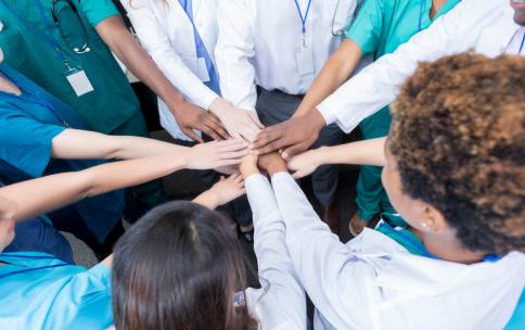  A diverse group of people wearing lab coats, scrubs, and business attire with their hands placed in the center to represent teamwork.