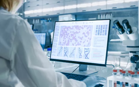 A scientist in a lab looking at an image of DNA on a computer screen.