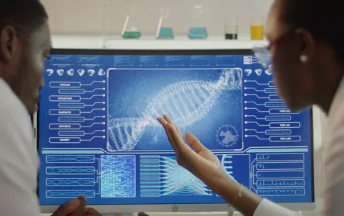 Two scientists looking at an image of DNA on a computer screen.